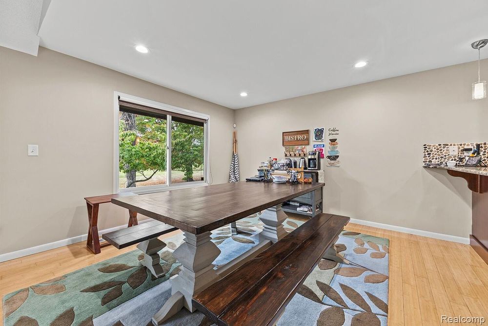 Dining room with dark wood farmhouse table, bench seating, blue leaf area rug, and sliding glass door to backyard.