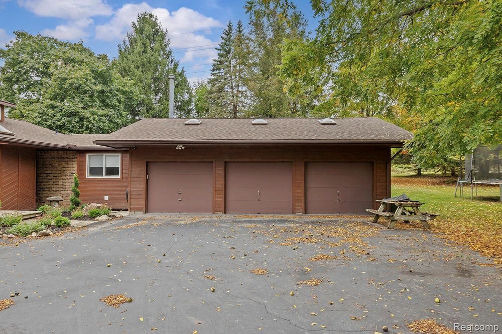 Three-car attached garage with brown doors, asphalt driveway, and mature trees surrounding home.