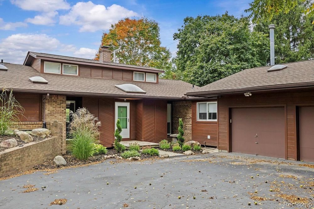 Mid-century modern brick home with green front door, attached garage, and mature landscaping.