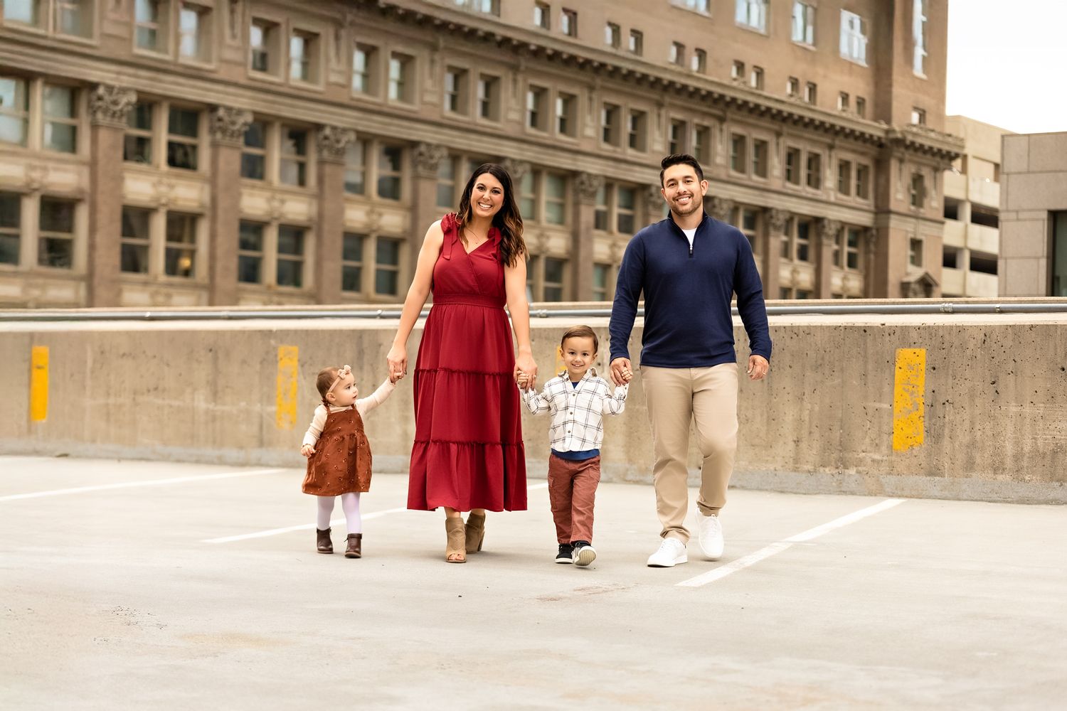 A family of four walks together on a rooftop parking deck with a brick building in the background.