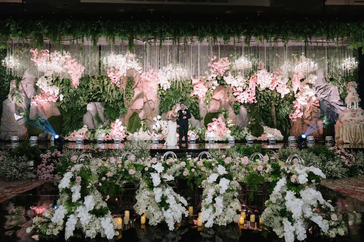 Stunning wedding venue stage decorated with pink orchids, greenery, and white floral arrangements.