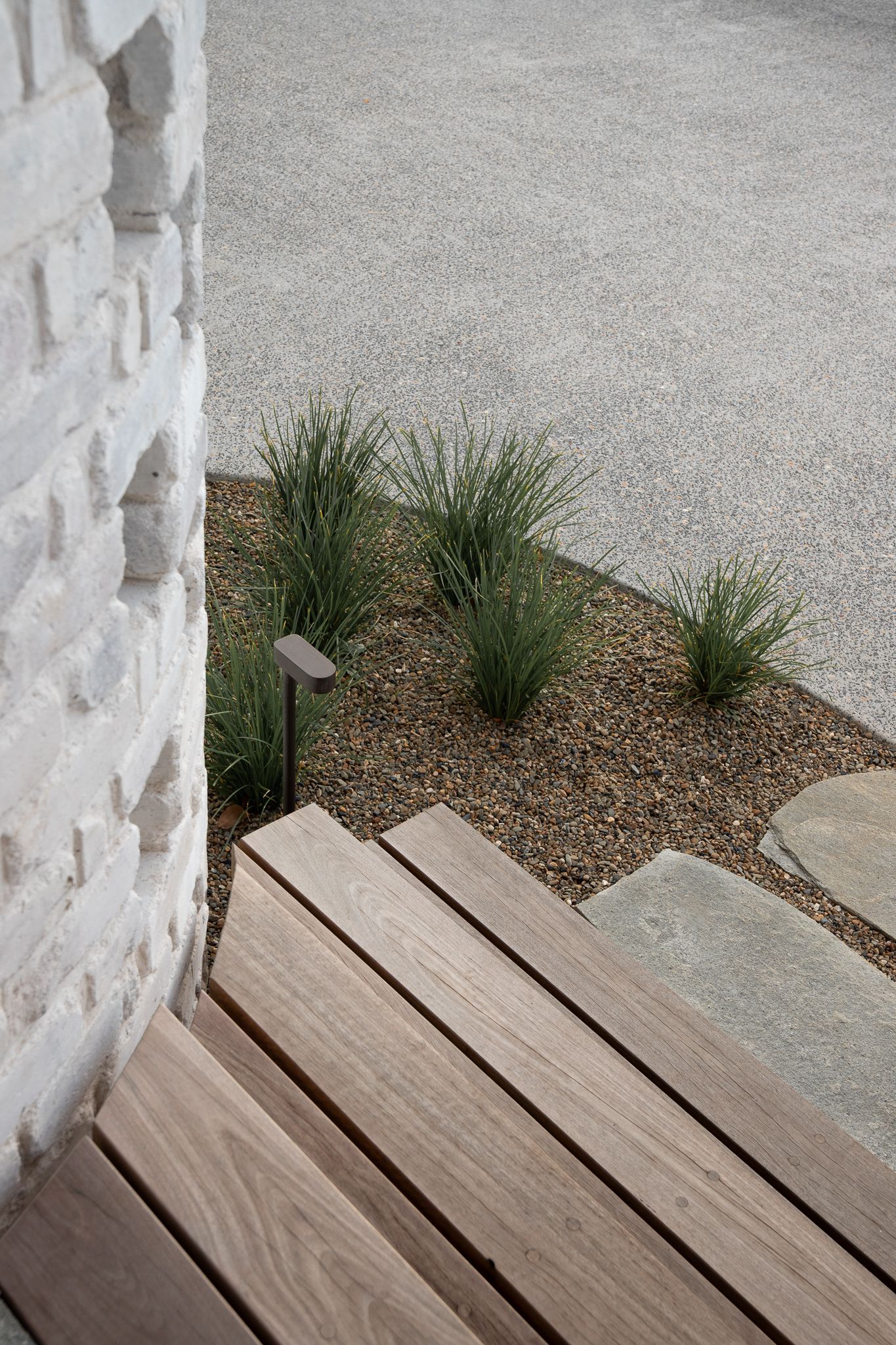 Minimalist outdoor decking with native grass landscaping and textured white columns.