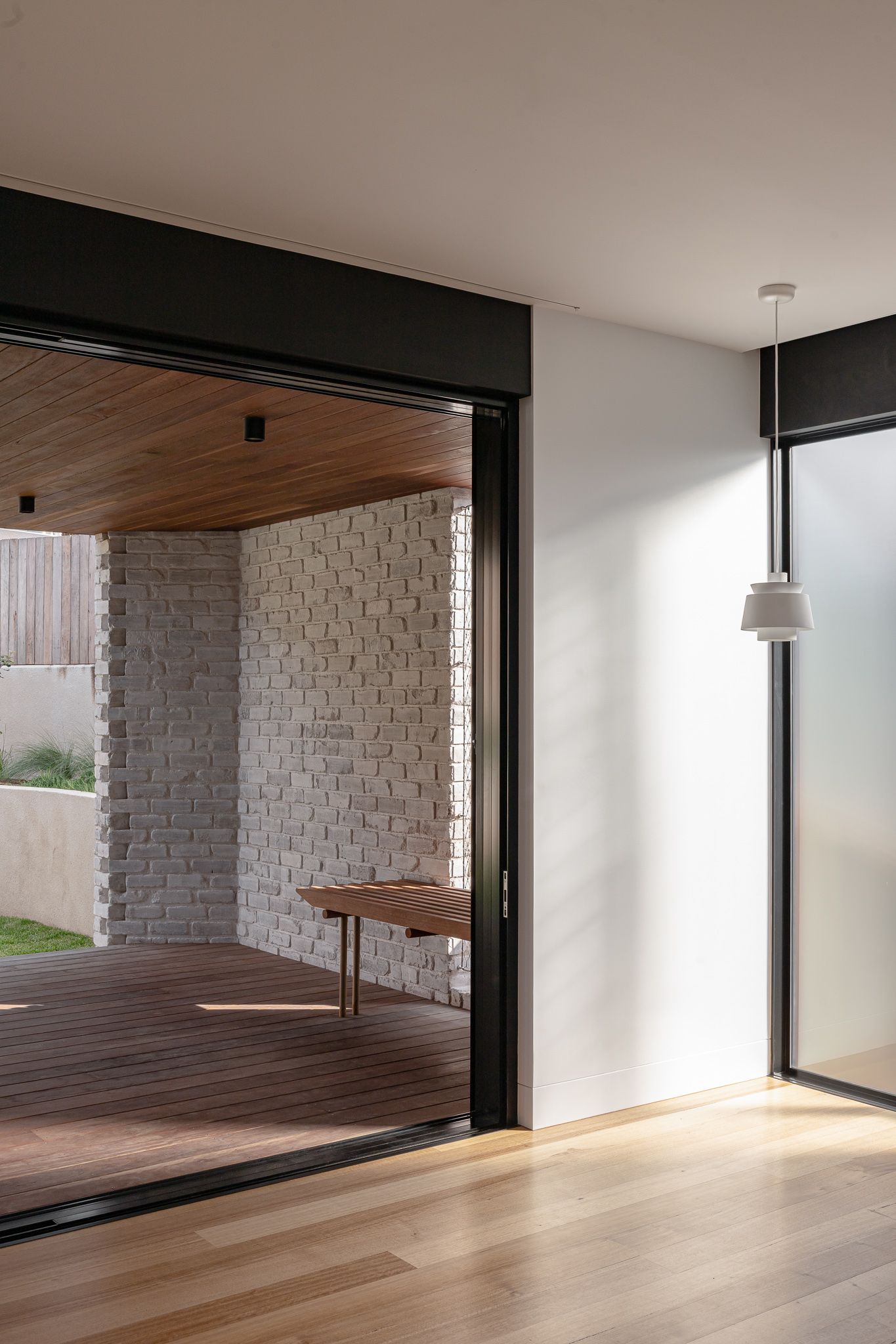 Modern living space with light wood floors connecting to covered outdoor deck through sliding glass doors.