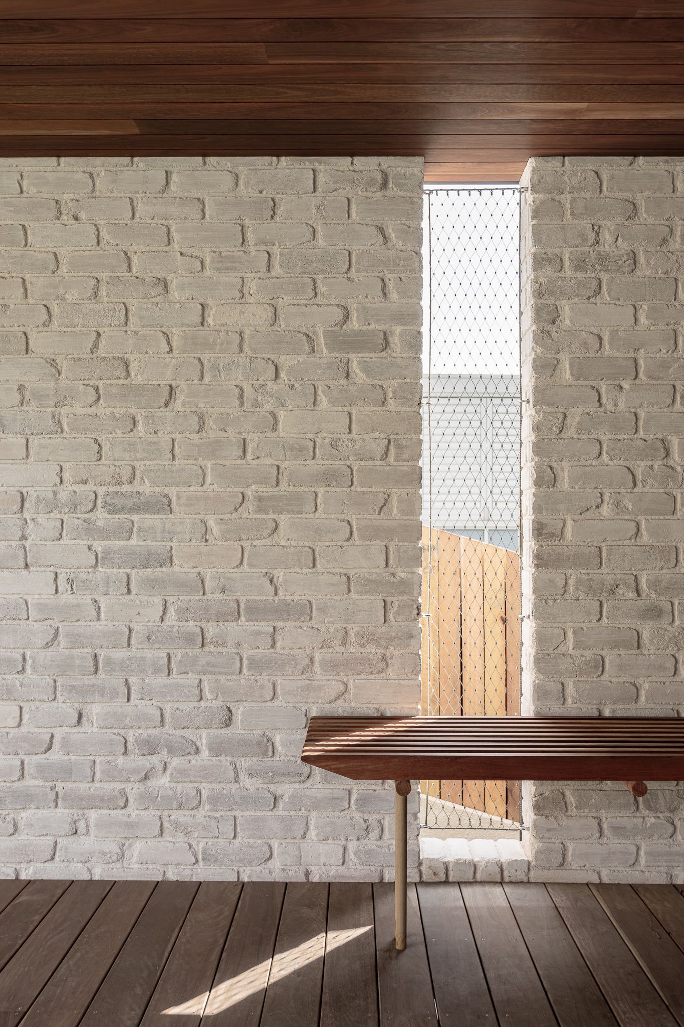 Sunlight streams through windows onto wooden floor in empty room with painted brick walls creating dramatic shadows.