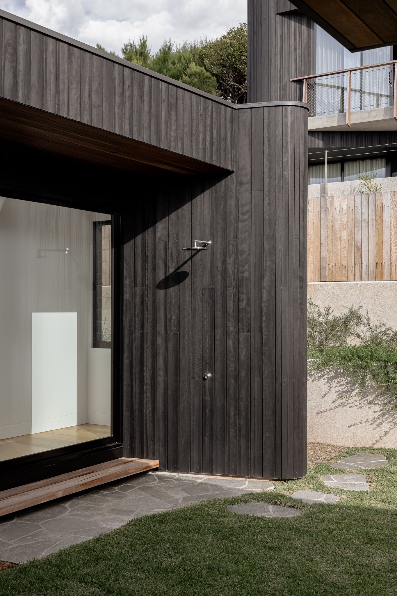 Modern black wood-clad building with minimalist design features white interior walls and wooden deck entrance.