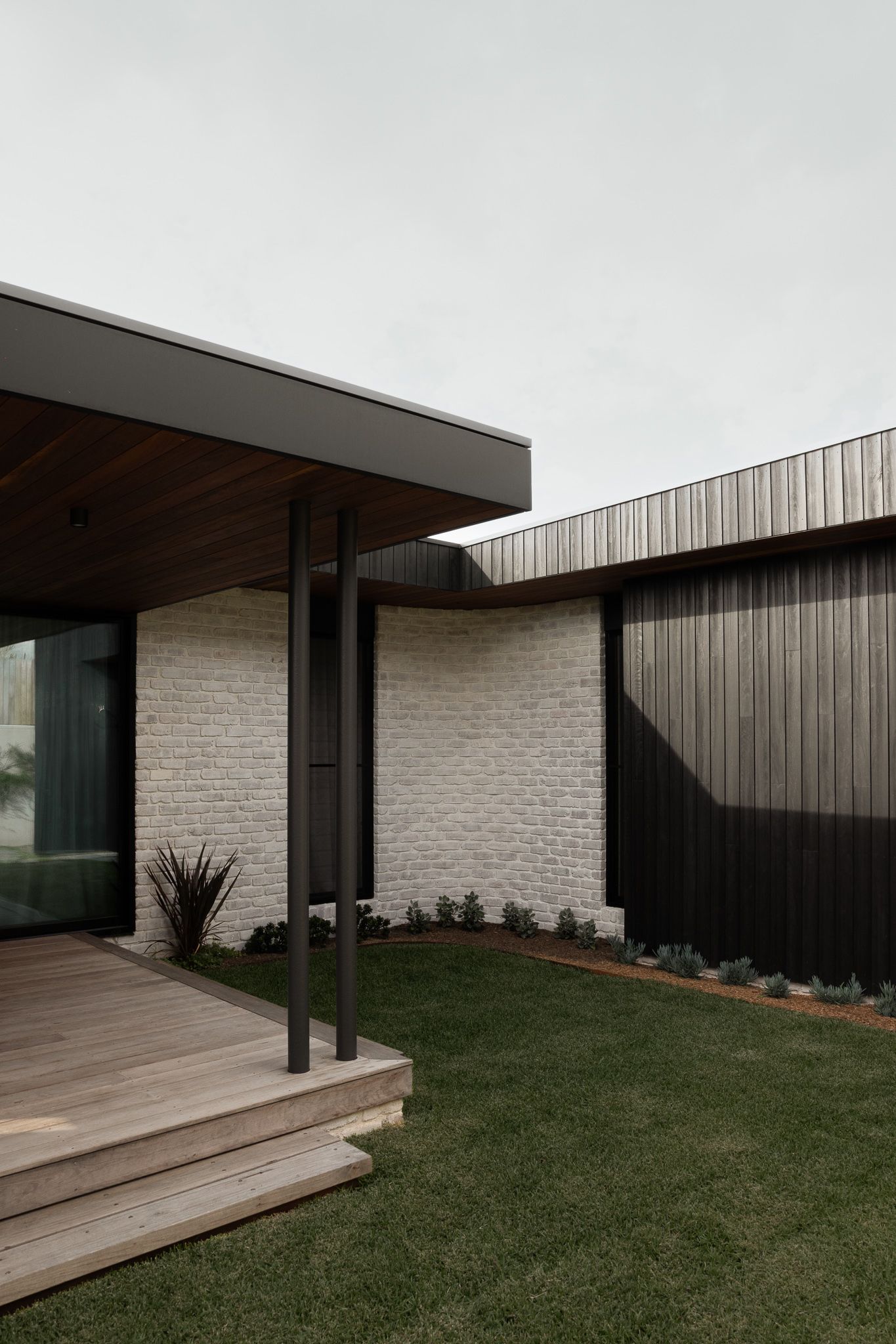Modern minimalist home exterior with white brick walls, dark wood cladding, and manicured lawn creating clean architectural lines.