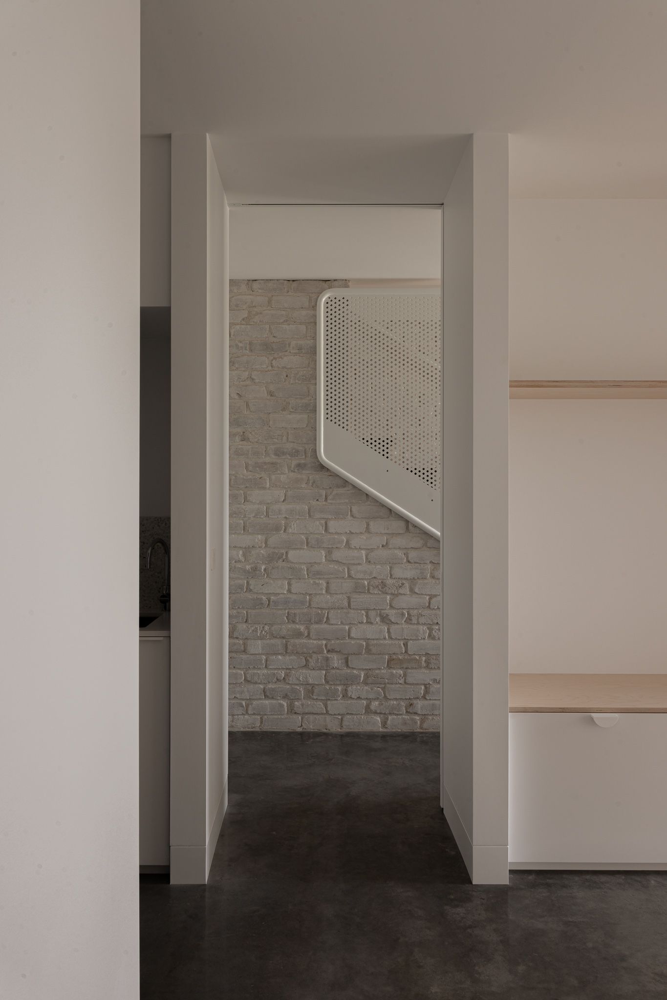 Interior view of a minimalist white basement space with exposed brick wall and staircase visible in the frame.