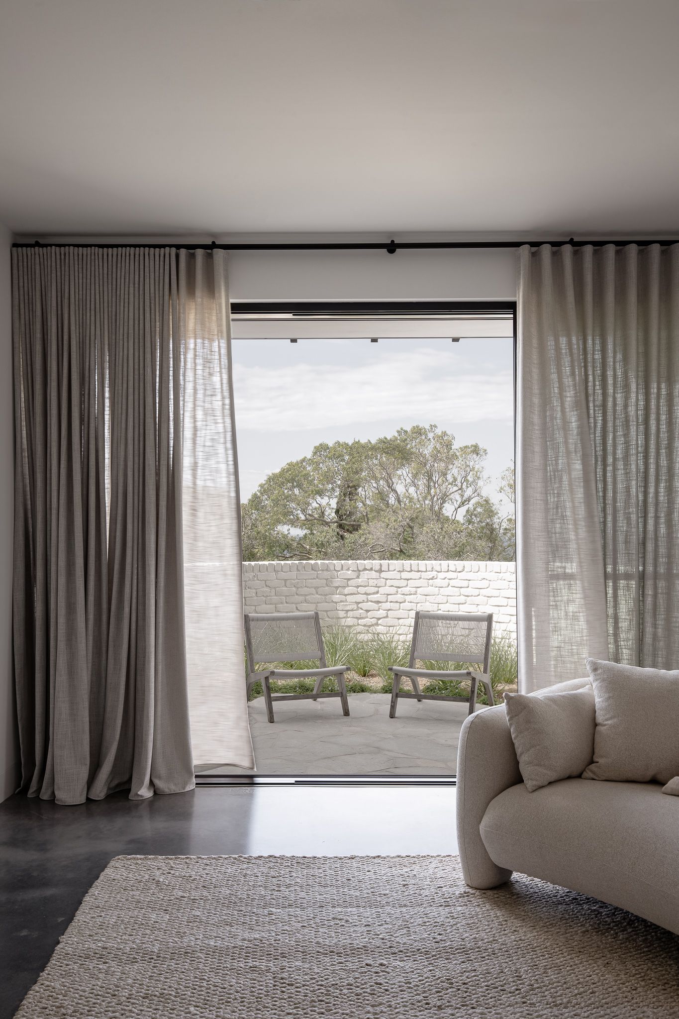 Modern living room interior with floor-to-ceiling windows, white curtains, and curved sofa offering panoramic outdoor views.