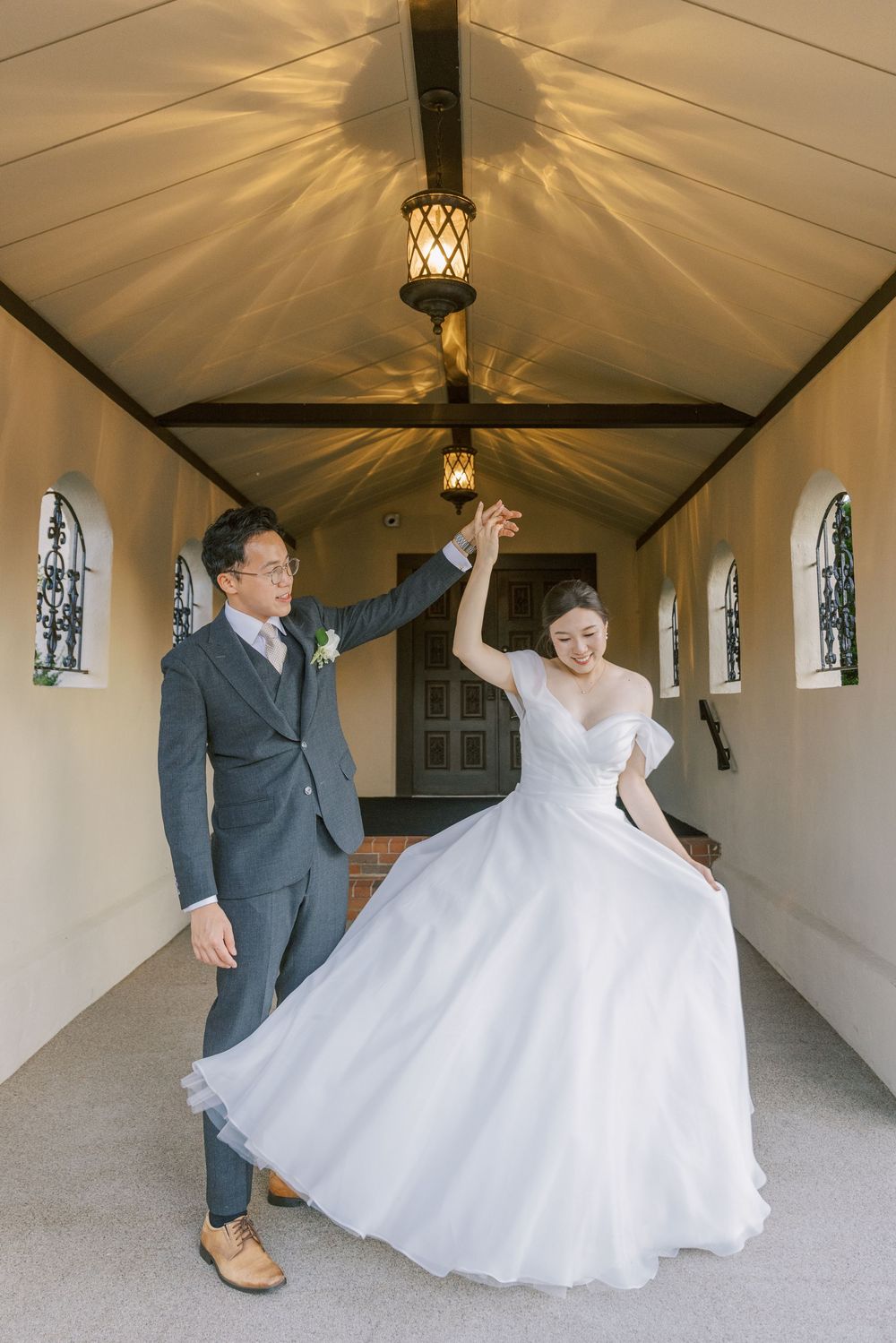 A couple dances joyfully in a chapel hallway with dramatic lighting and stained glass windows.