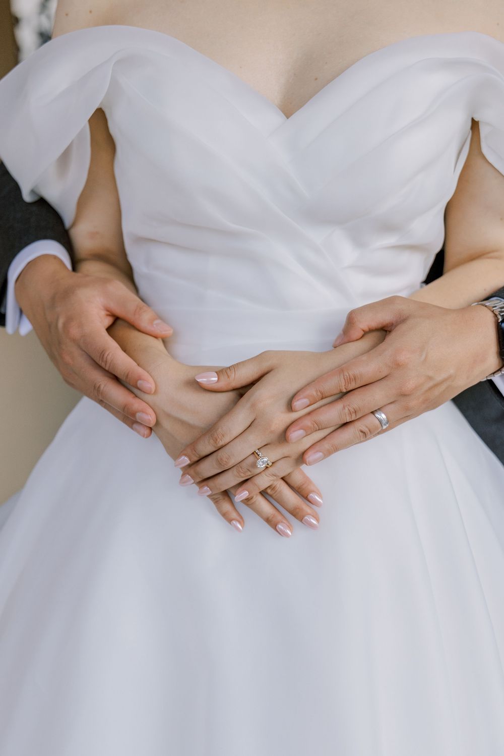 Close-up shots of hands with manicured nails clasped together against a white wedding dress.