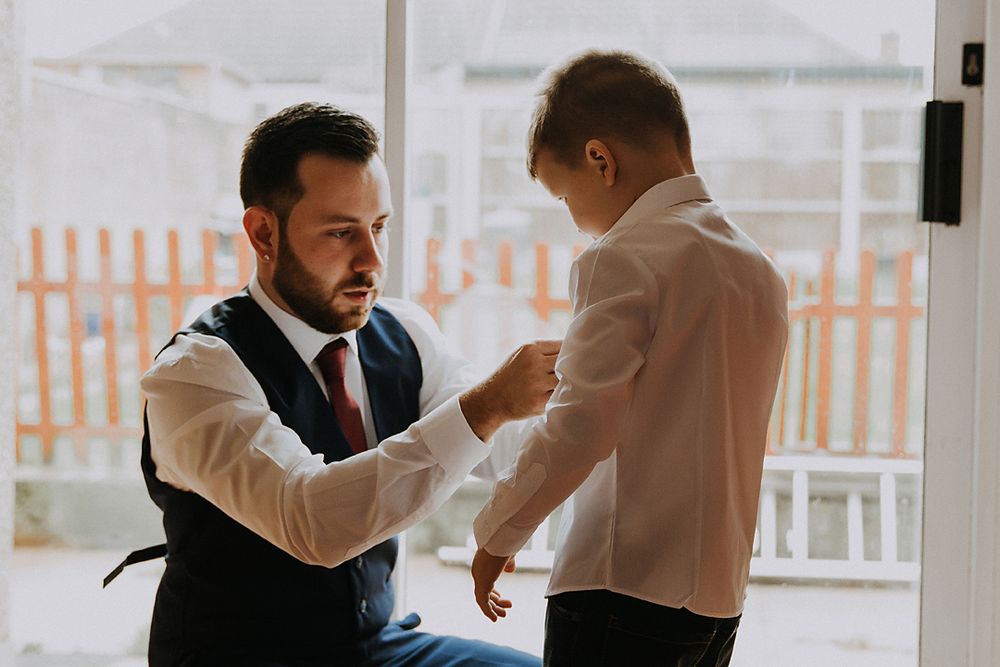 groom and his son standing by a bright window fixing his sons tie
