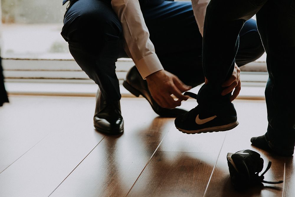A person in black pants and white sneakers crouches down on a light colored floor.