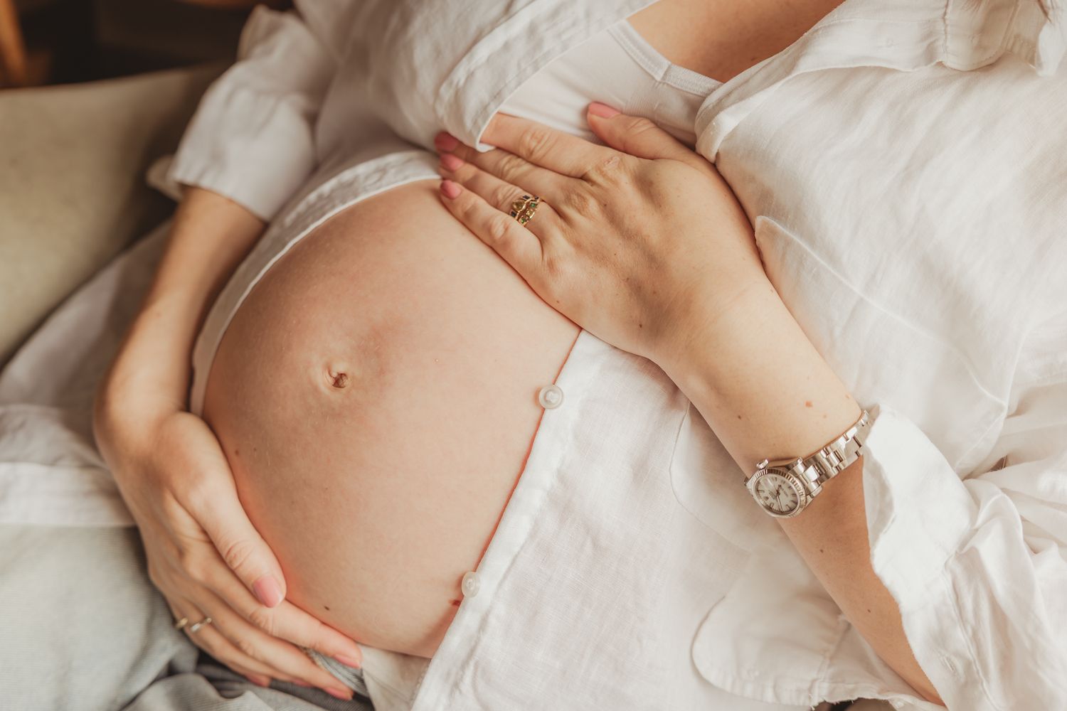 Close-up shots of a pregnant belly with gentle hands cradling it against white fabric.