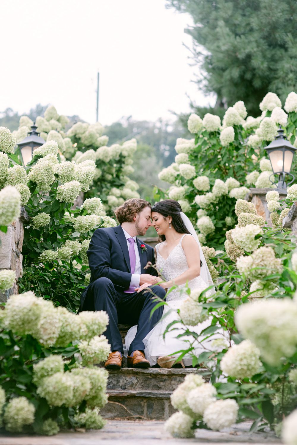 A romantic moment captured in a garden setting surrounded by lush white hydrangea blooms on a summer day.
