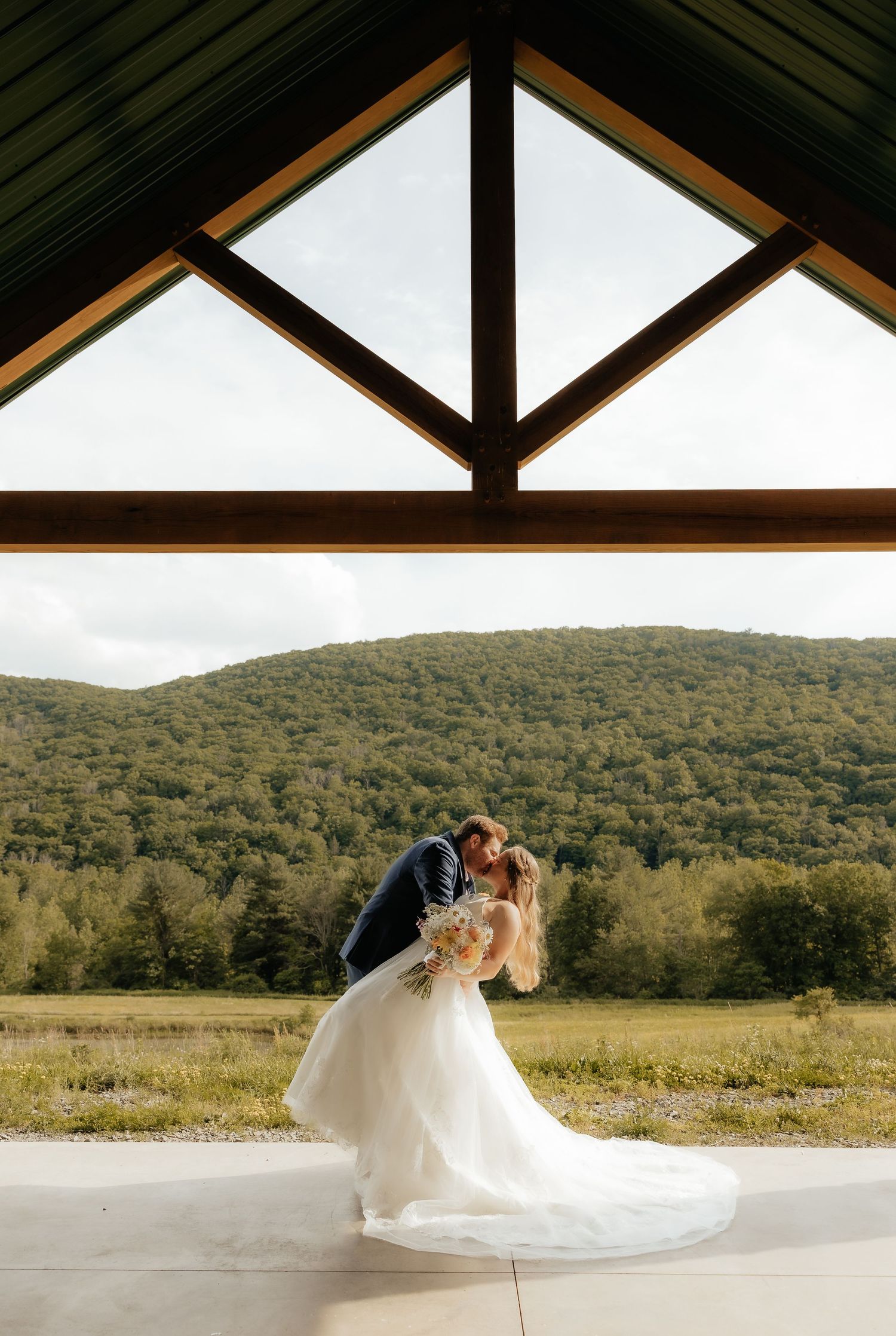 A romantic wedding photo session on a grassy lakeside with water and trees in the background.
