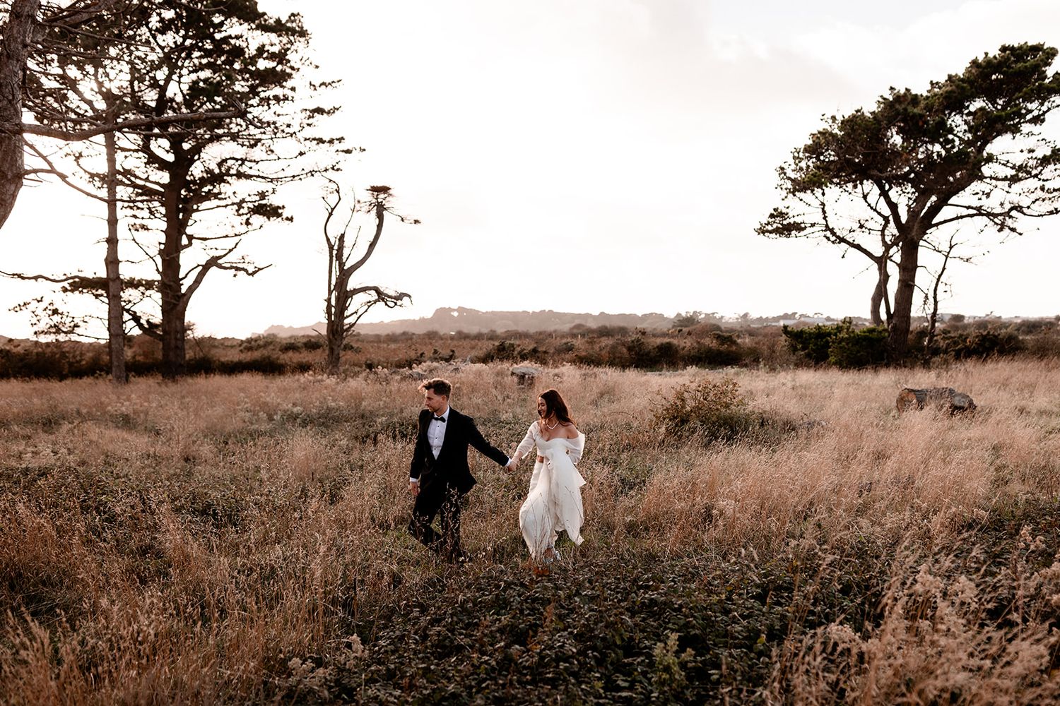Sepia-toned landscape with couple walking among sparse trees in open field.