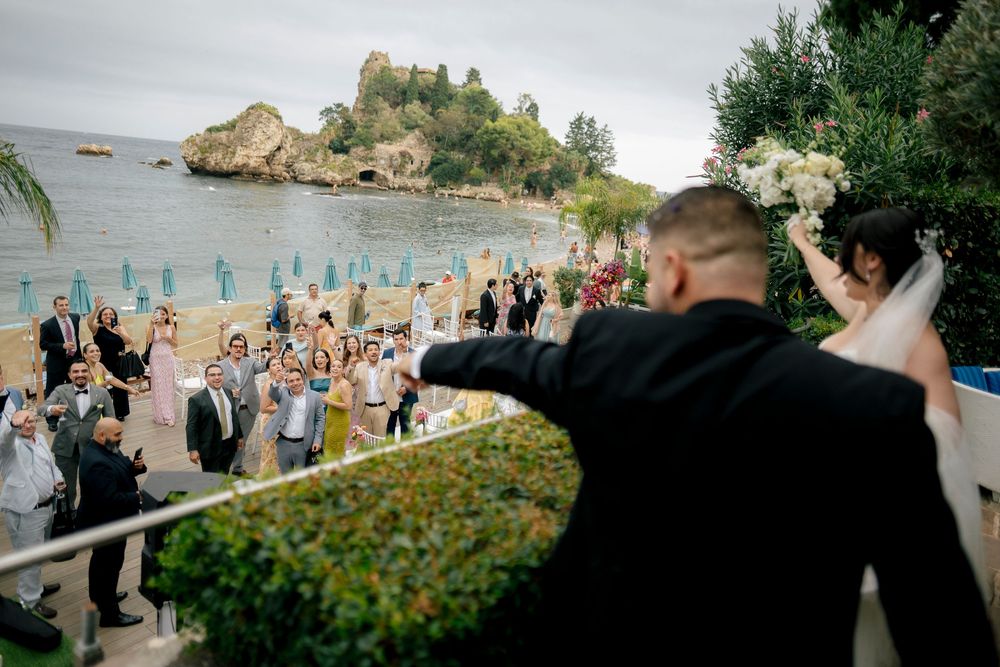 A wedding celebration overlooking the beautiful Isola Bella island in Taormina, Sicily with guests gathered below.