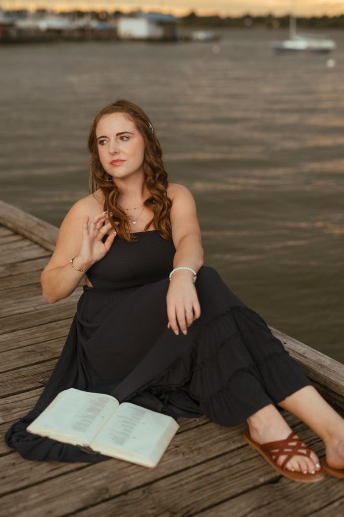 Sunset portrait session on a dock featuring a black maxi dress and open book.