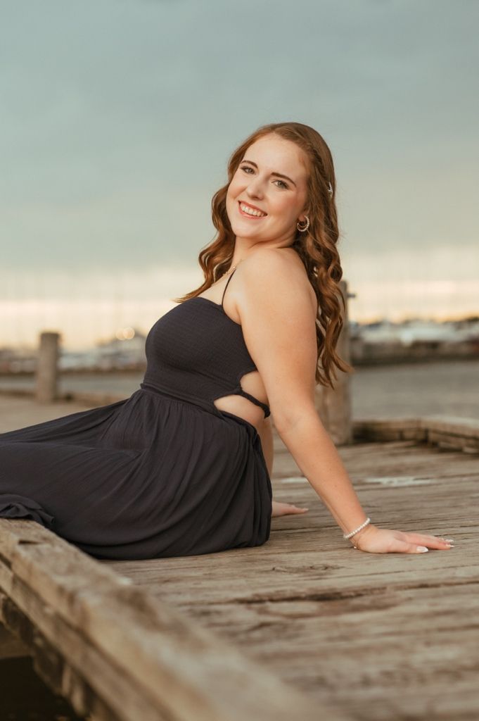 A black dress is modeled on a rustic wooden dock during golden hour.