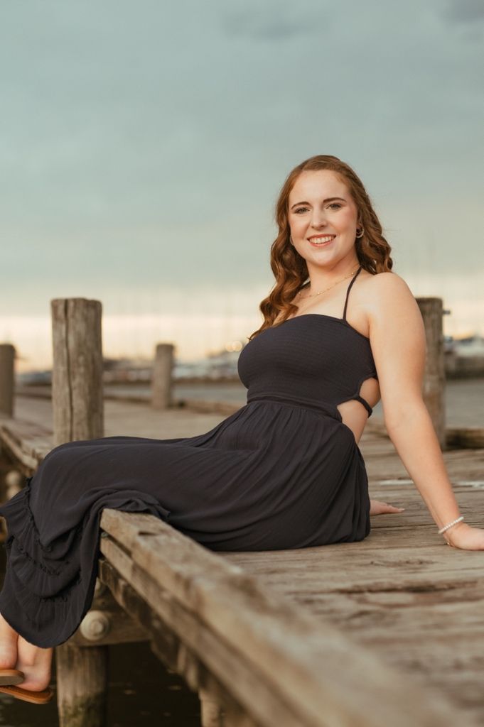 Person in black dress lounging on wooden pier during golden hour.