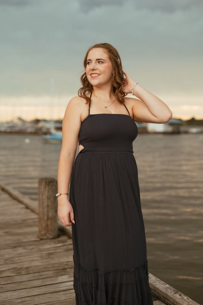 A flowing black maxi dress is displayed against a waterfront backdrop on a wooden pier.