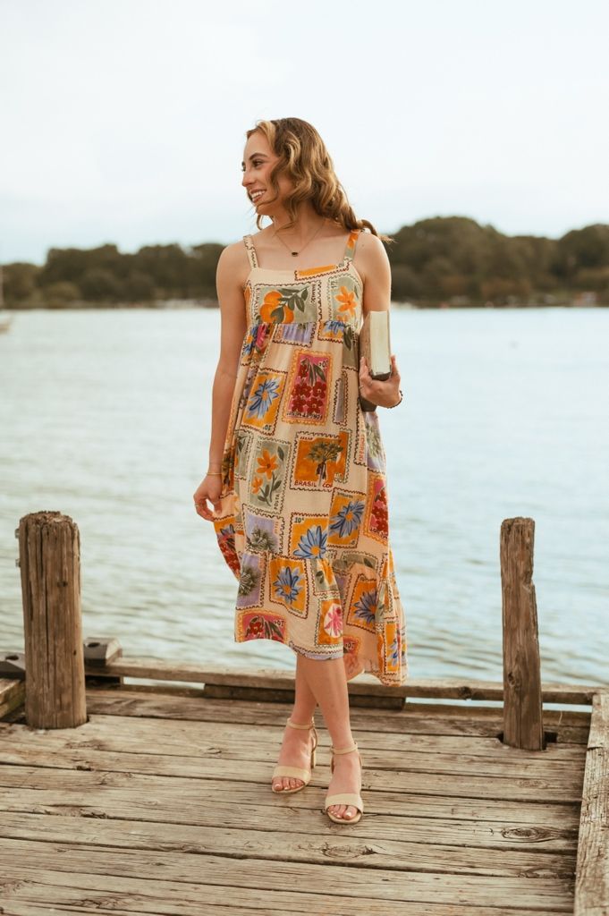 Woman in colorful patterned sundress poses on wooden dock by lake during sunset photoshoot.