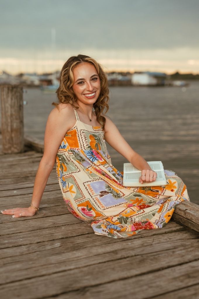 A colorful printed sundress is showcased on a wooden dock at sunset with water in the background.