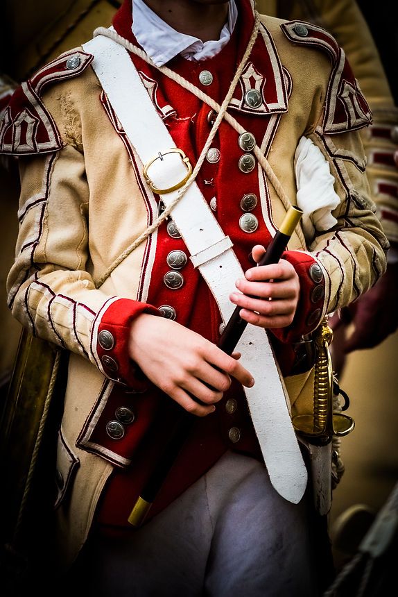Historical reenactor in ornate 18th century military uniform holding a sword during a period event.