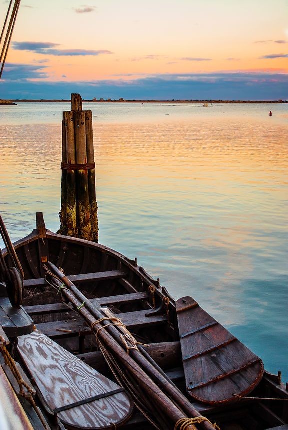 Rustic wooden rowboat docked at a pier during a serene golden sunset over calm water.