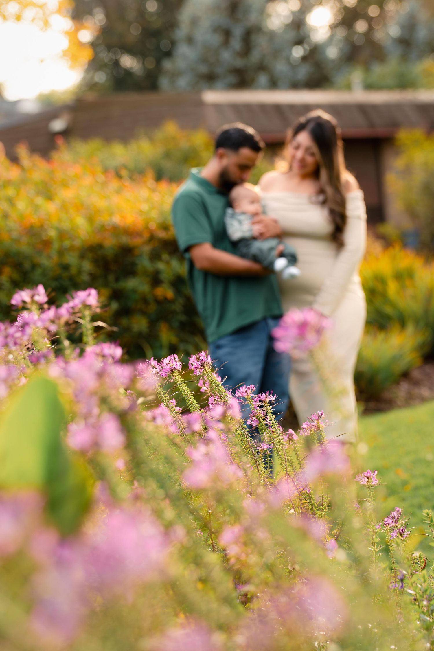 Couple standing in garden with pink flowers in foreground during sunset.