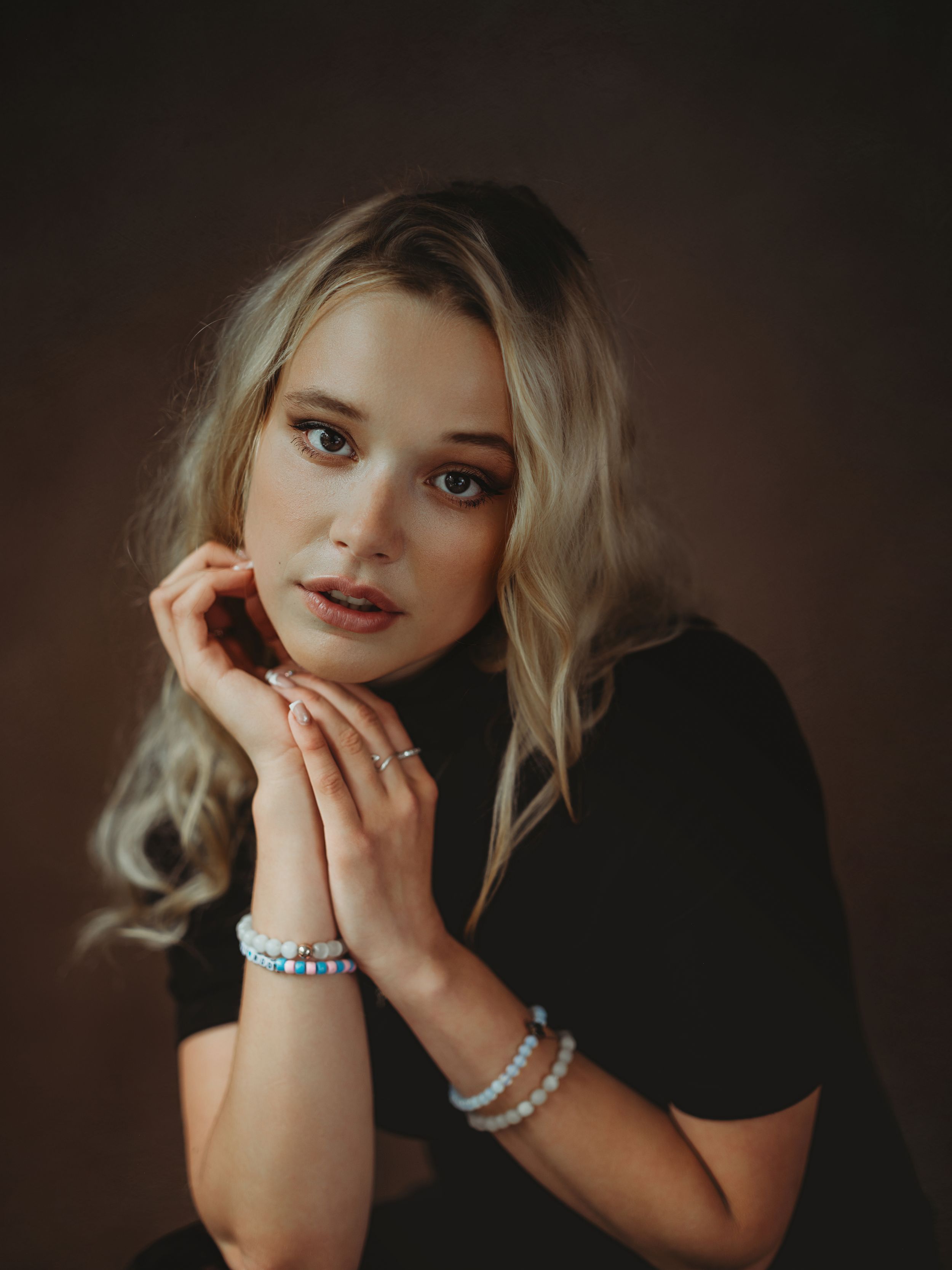 A moody portrait series featuring dramatic lighting and elegant pearl jewelry against a dark background.