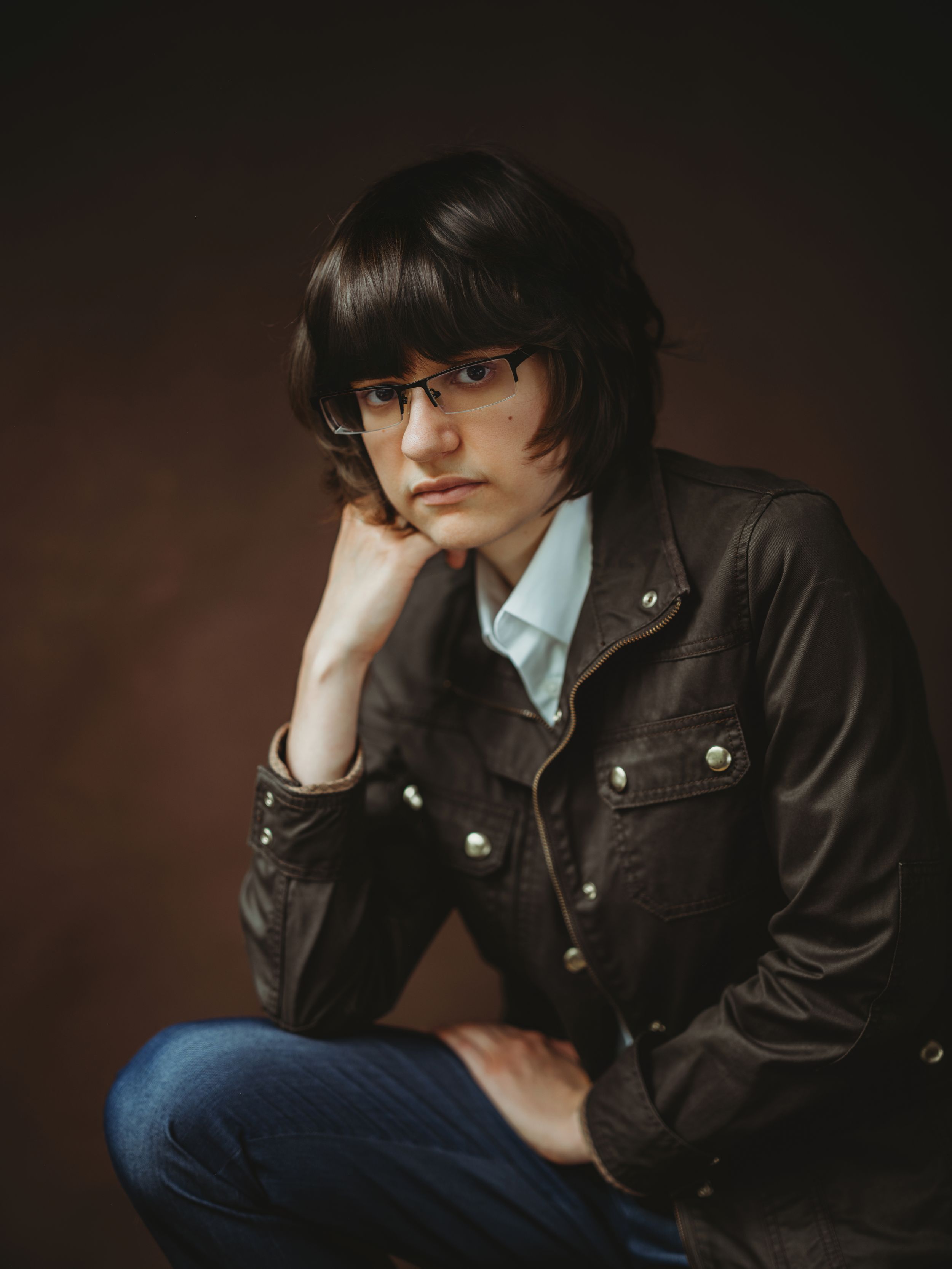 Portrait series in dark tones showing a figure in a leather jacket and glasses against a brown background.