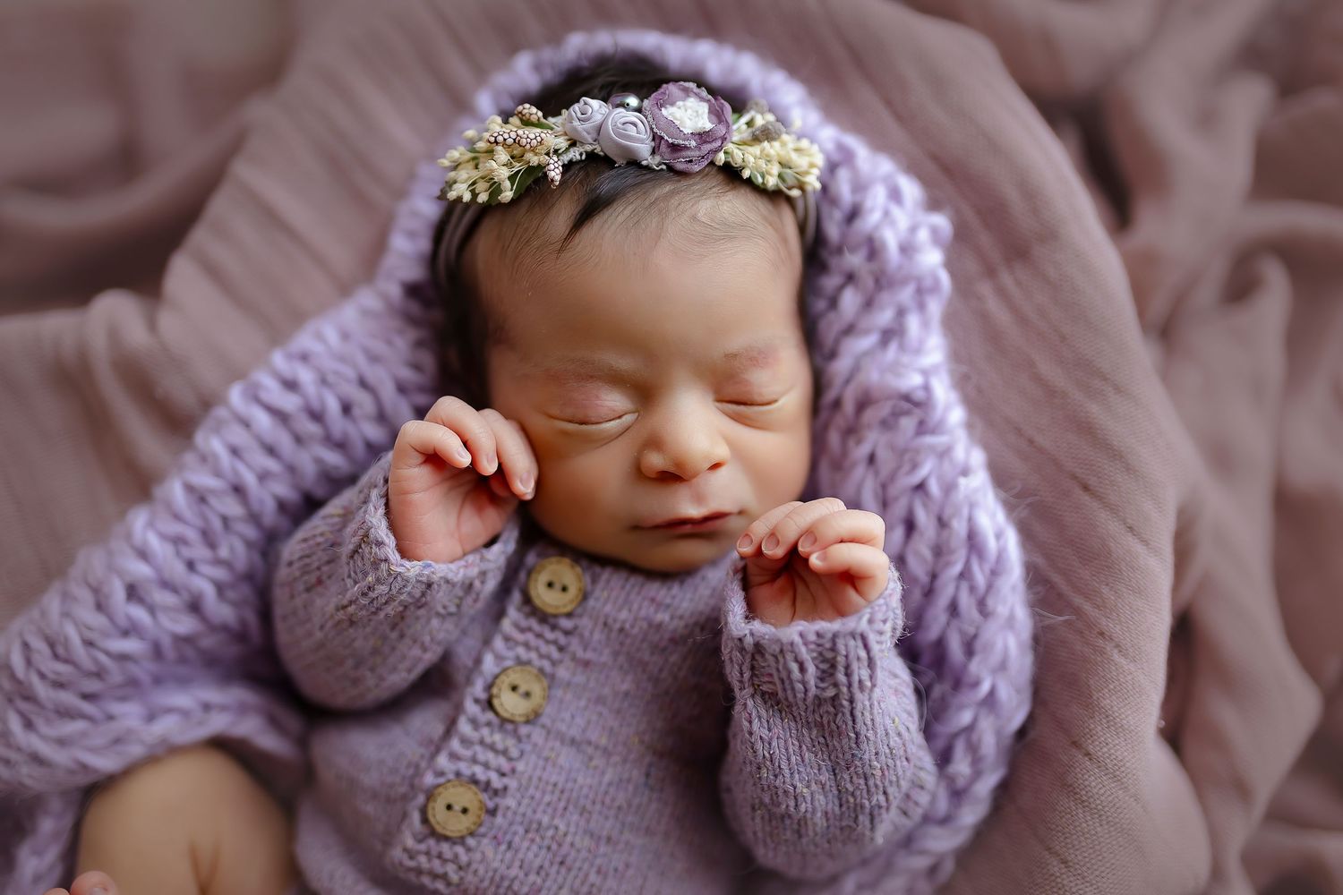 Fotografia de bebe recien nacida durmiendo con las manitas cerca de su rostro vestida de color lavanda