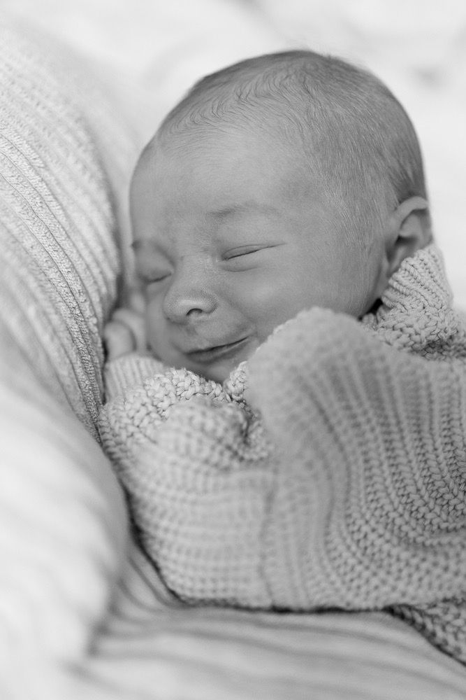 Black and white portrait of a newborn baby sleeping peacefully while wrapped in a knit blanket.