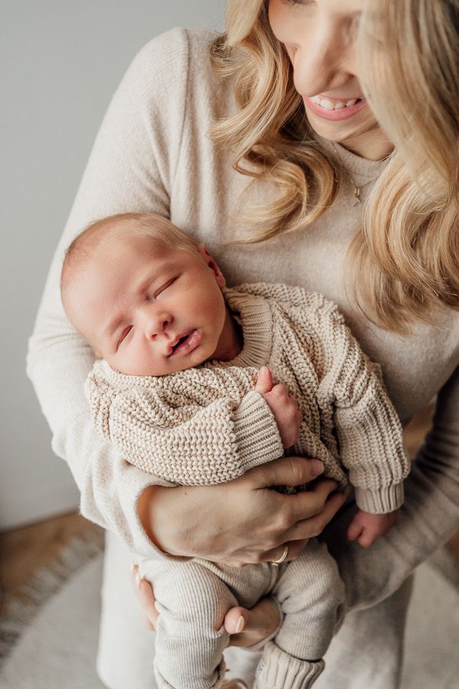 Tender newborn photography series showing sleeping baby in neutral knit sweater cradled against parent in soft lighting.