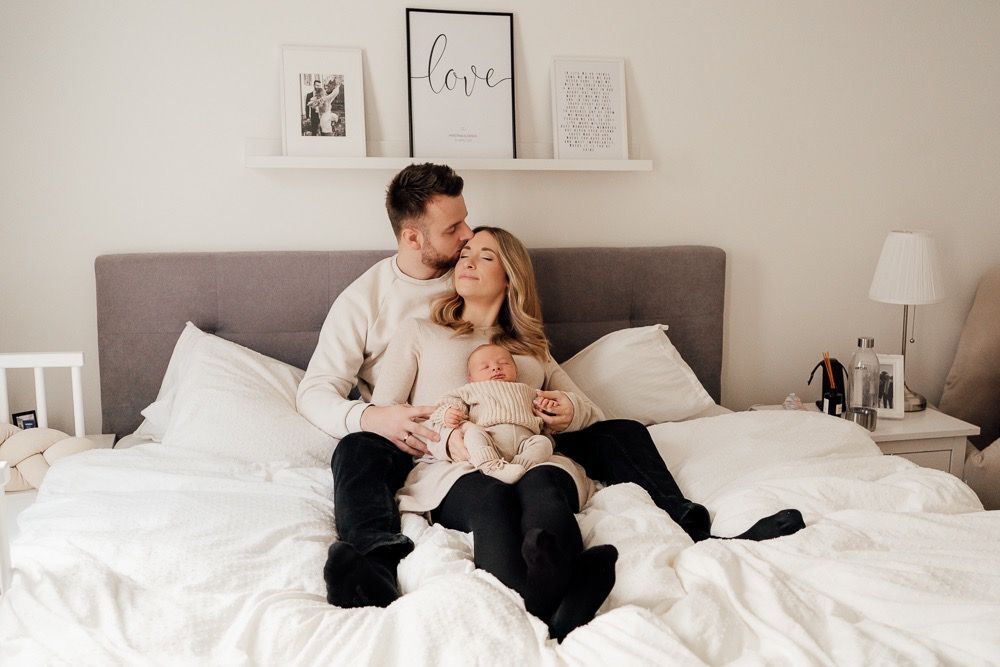 Couple relaxing together in white bedding while using mobile phones and electronic devices.