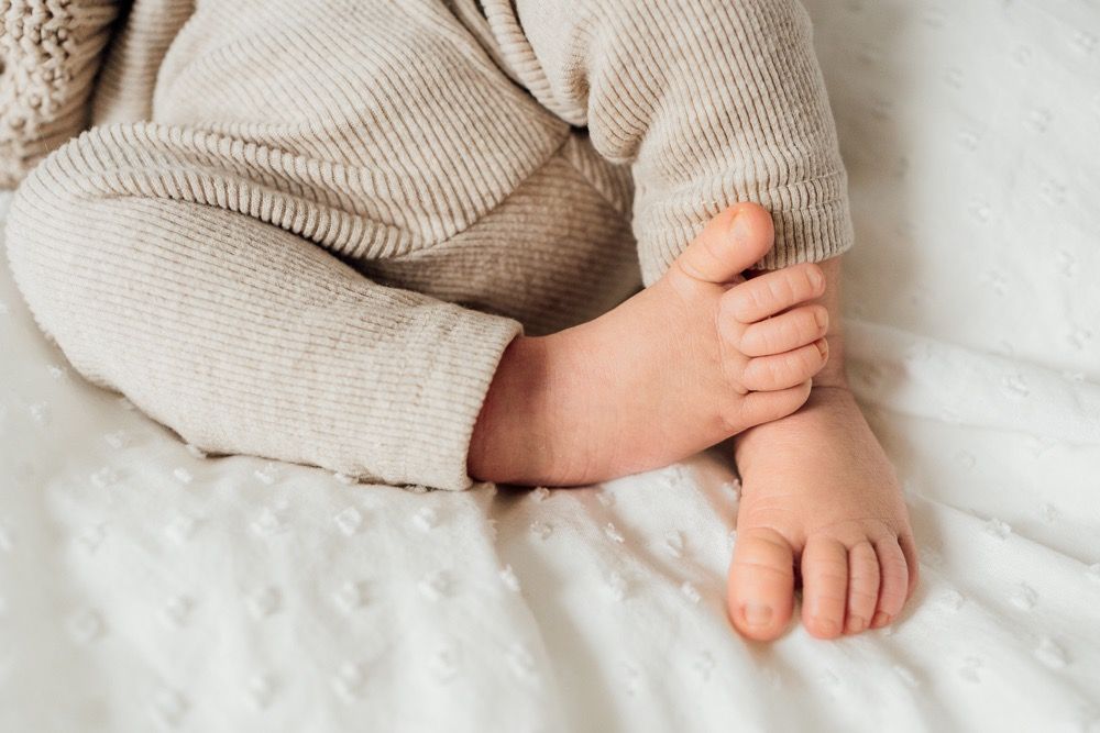 Small bare baby feet resting on soft white bedding showing delicate toes and skin texture.