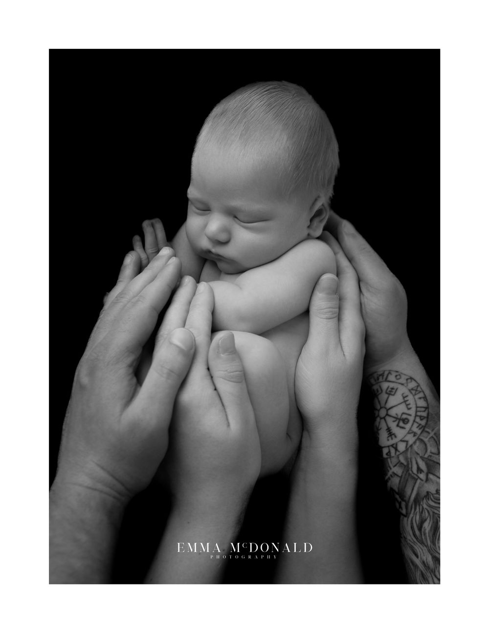Artistic black and white portrait of a sleeping newborn baby cradled in adult hands.