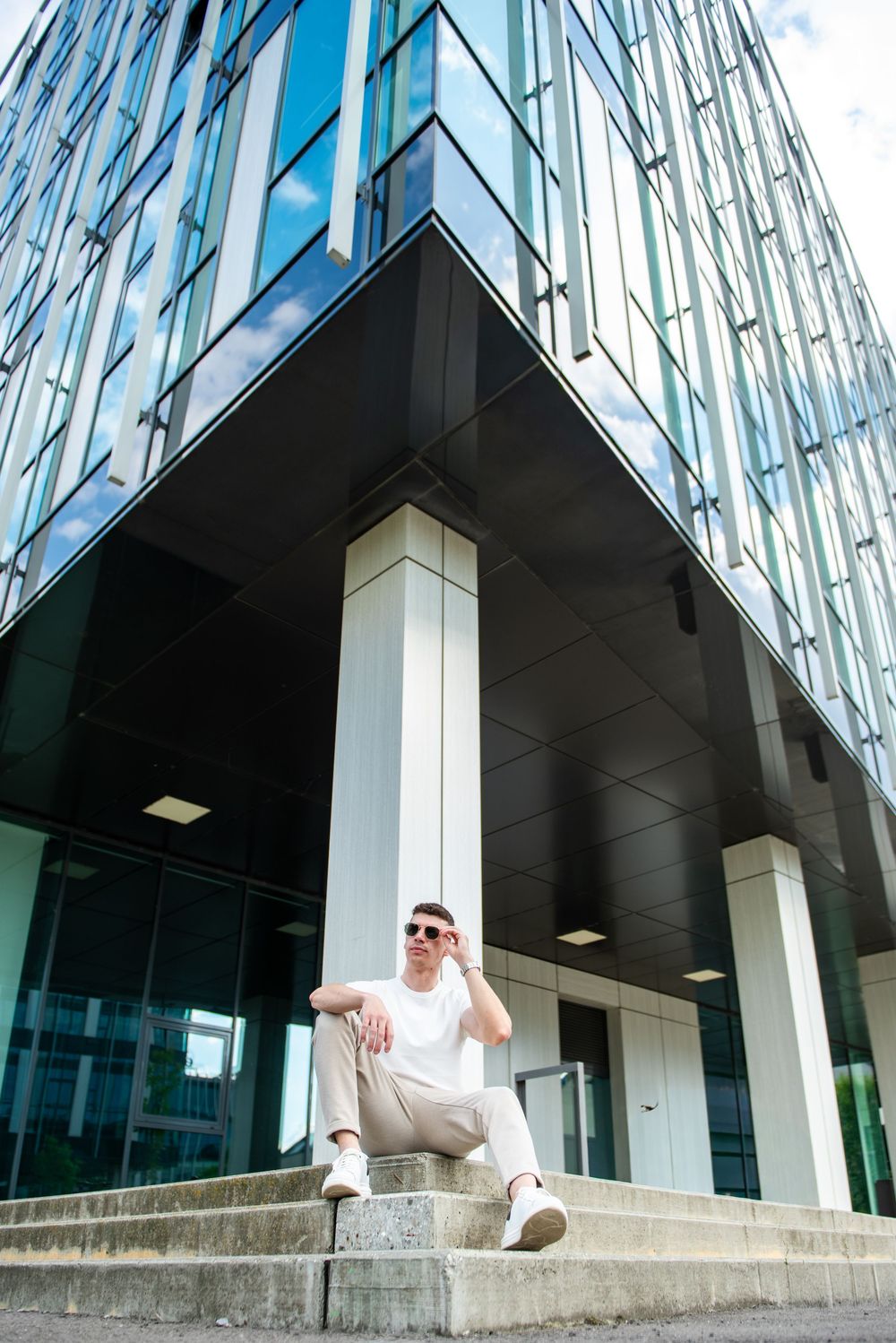 Modern glass building facade with geometric patterns and angular architectural details creates striking reflections.