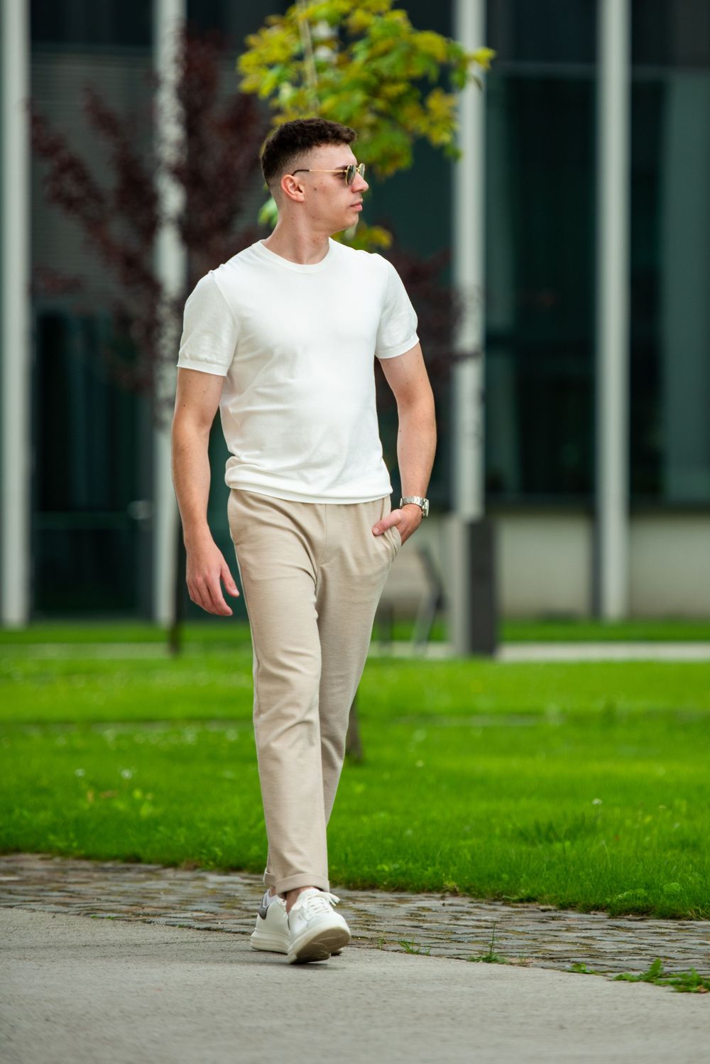Person in white t-shirt and beige pants walking on a path near a grassy area in a casual outdoor setting.