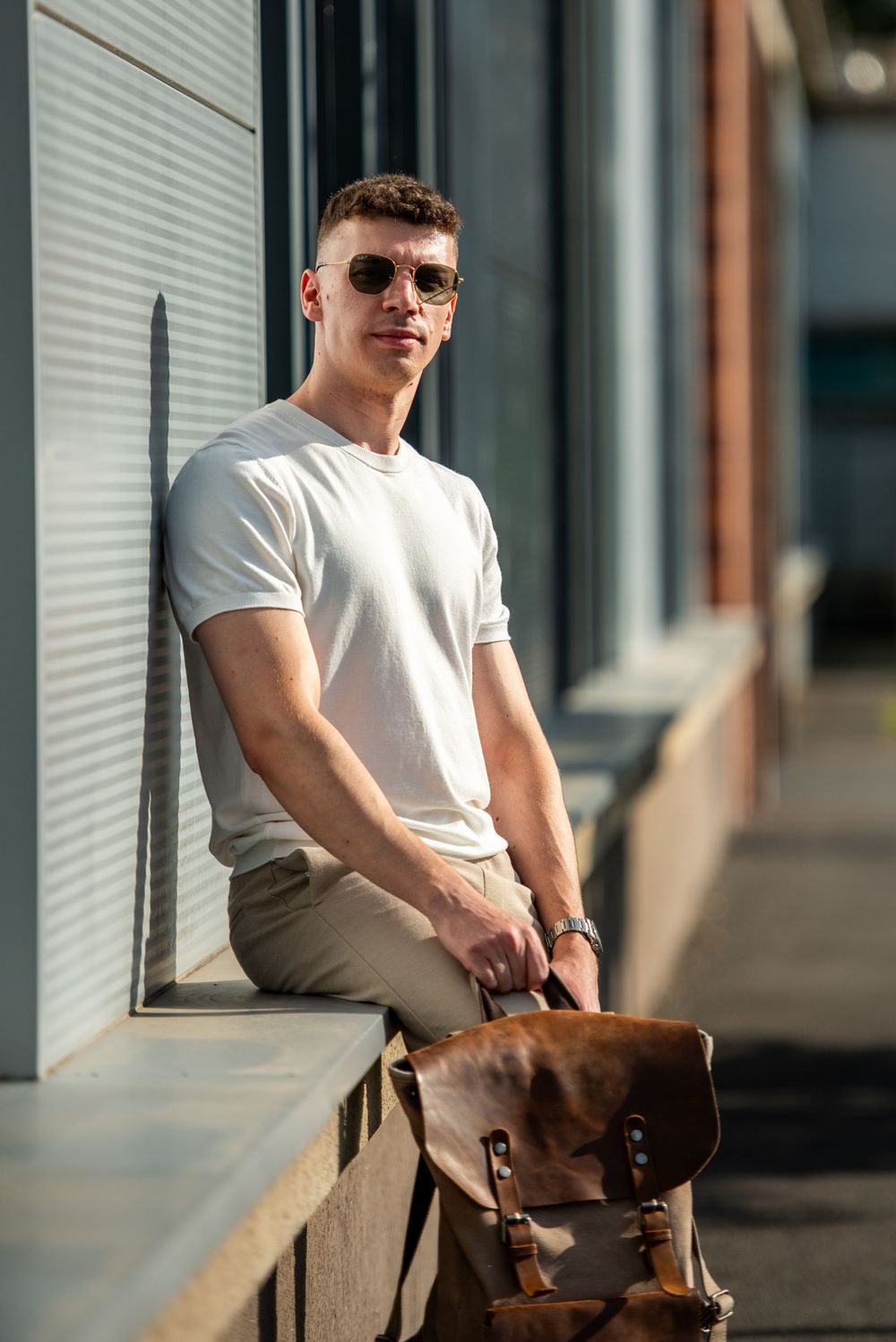 Person in casual attire with sunglasses sits on concrete ledge against industrial metal siding backdrop.