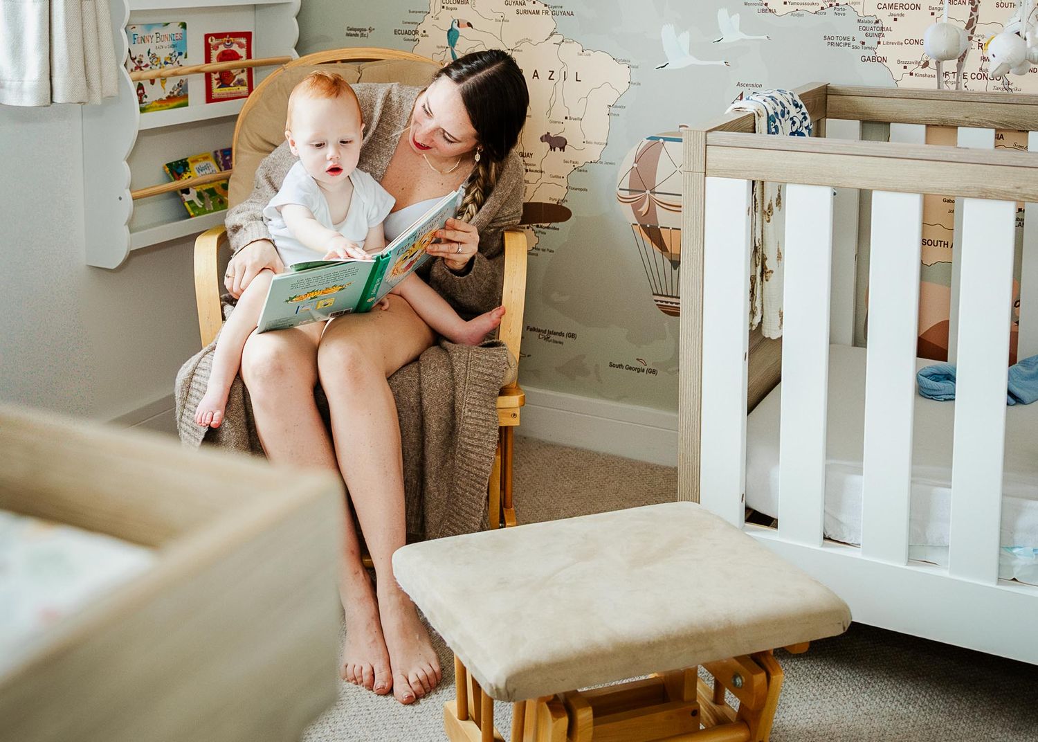 A mother looks relaxed in the nursery at home as she reads to her toddler. He points to a picture in the book. Bristol baby photographer