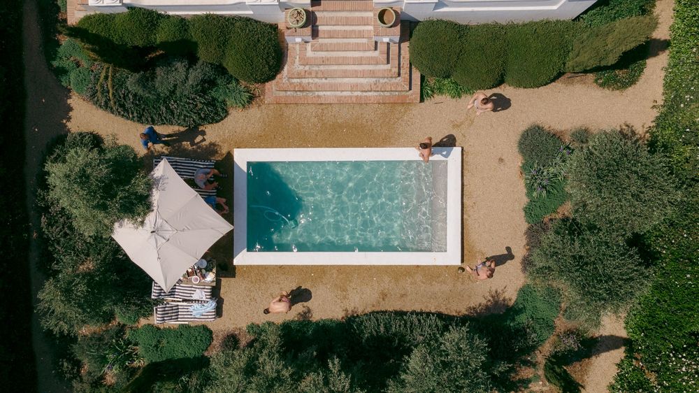 Aerial view of a luxury backyard swimming pool with surrounding landscaping and patio furniture.