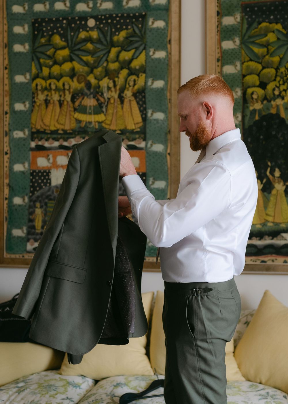 A person in a white dress shirt and dark pants inspects a black suit jacket against a backdrop of decorative wall art.