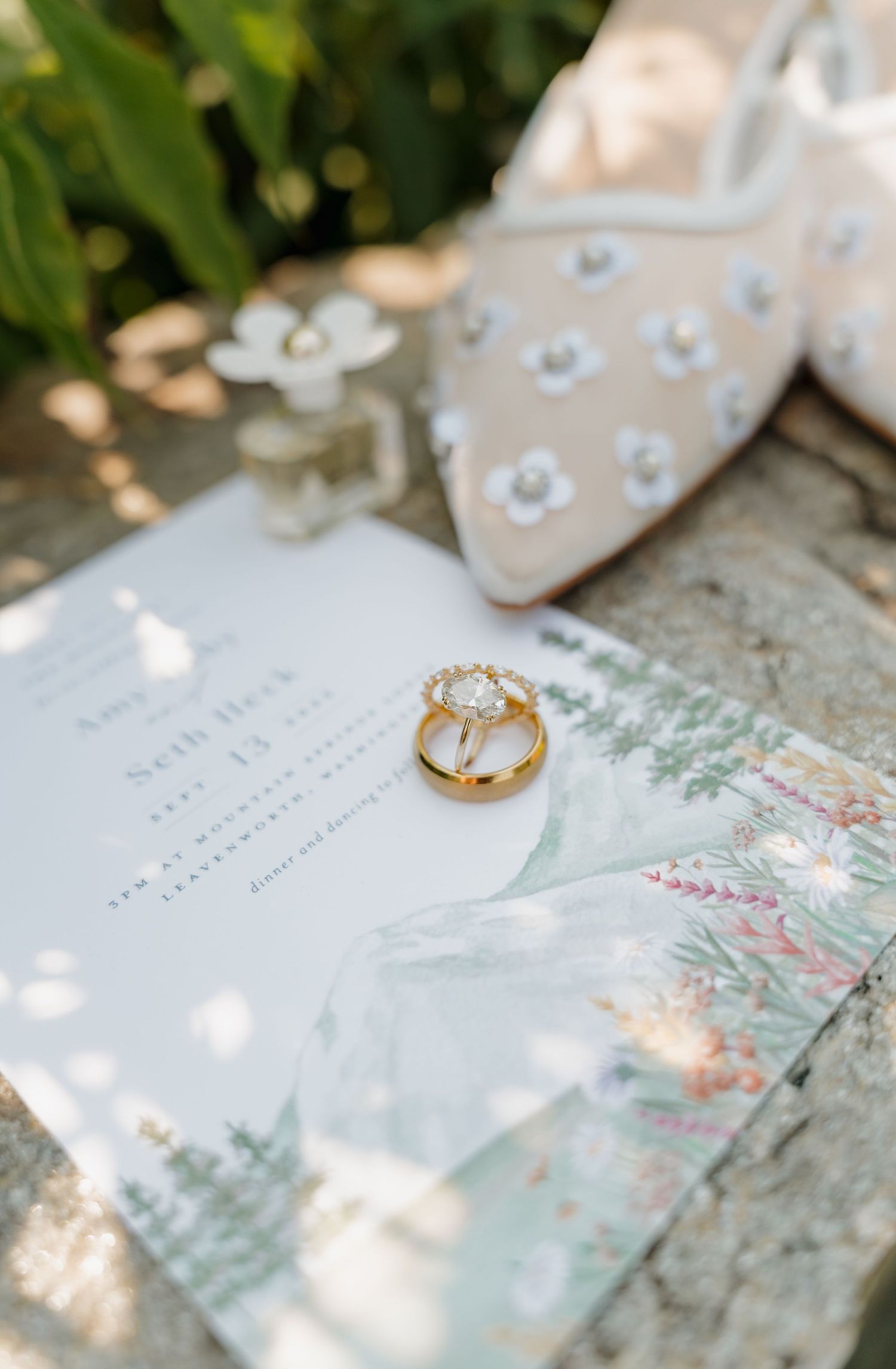 Wedding invitation with gold ring and floral details alongside embellished bridal shoes in natural lighting.