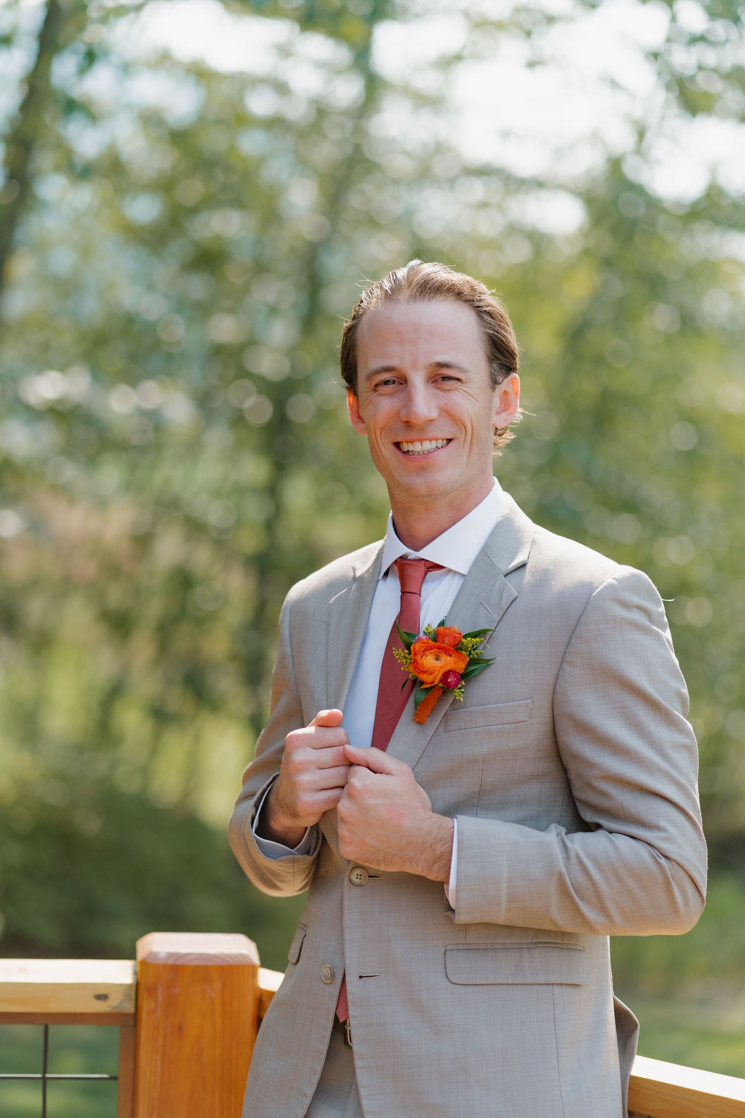 A series of four photos showing a person in a light gray suit with an orange boutonniere adjusting their tie outdoors.