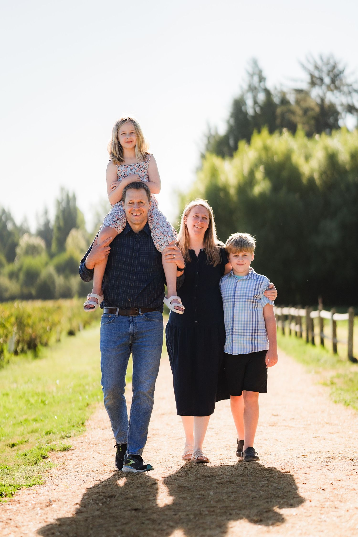 A family walks together on a sunlit dirt path through a scenic outdoor setting.