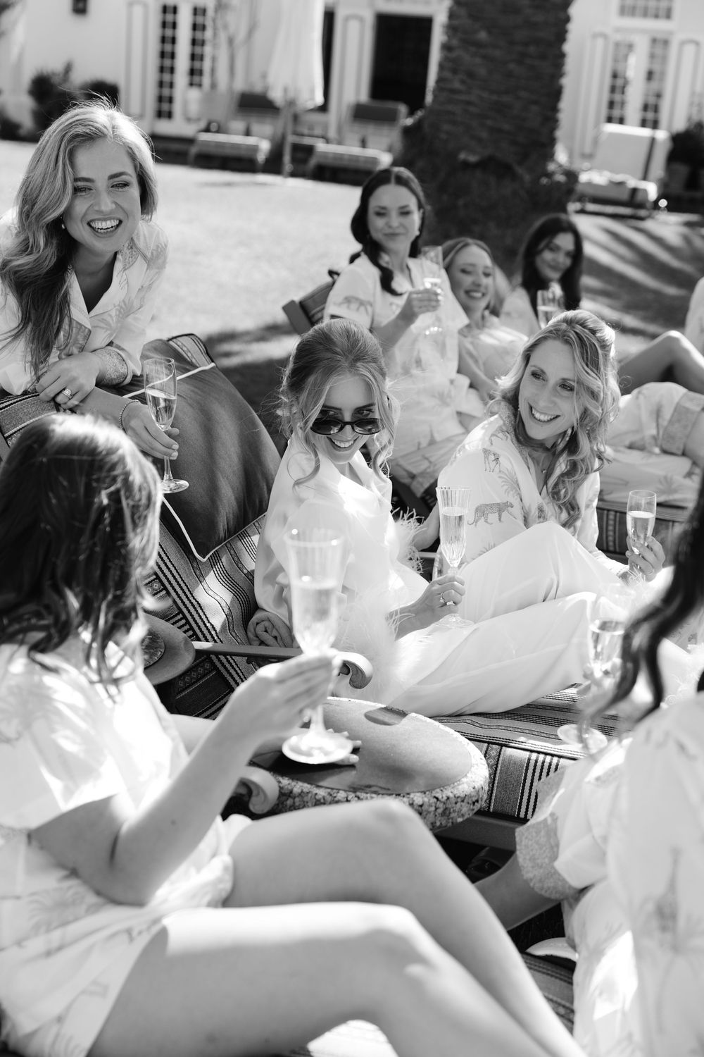 A candid black and white photo of a group in white outfits sitting together outdoors with a guitar.