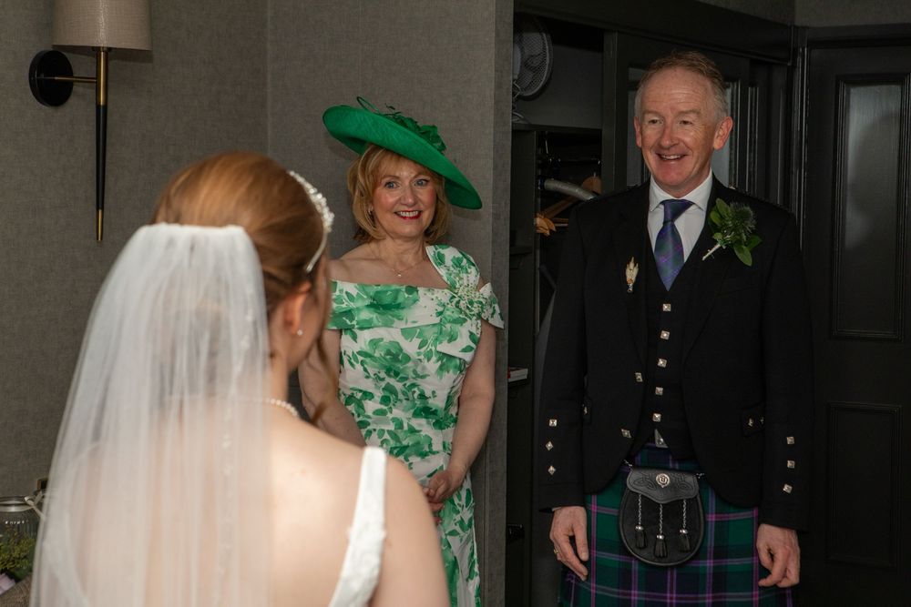 Wedding party members in formal attire and green dresses pose together at a celebration.