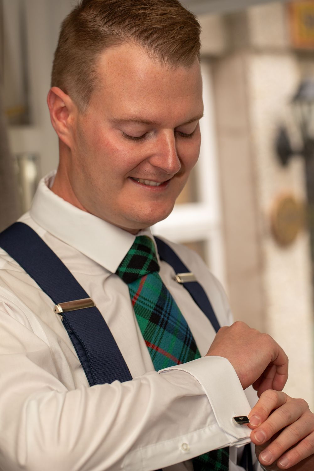 A person in a white dress shirt and green plaid tie adjusts their navy vest while getting dressed.